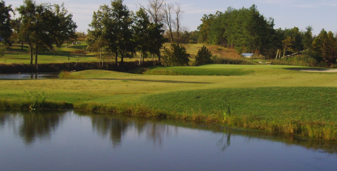 A landscape view of Panther Creek Golf Course including a pond and lush green grass